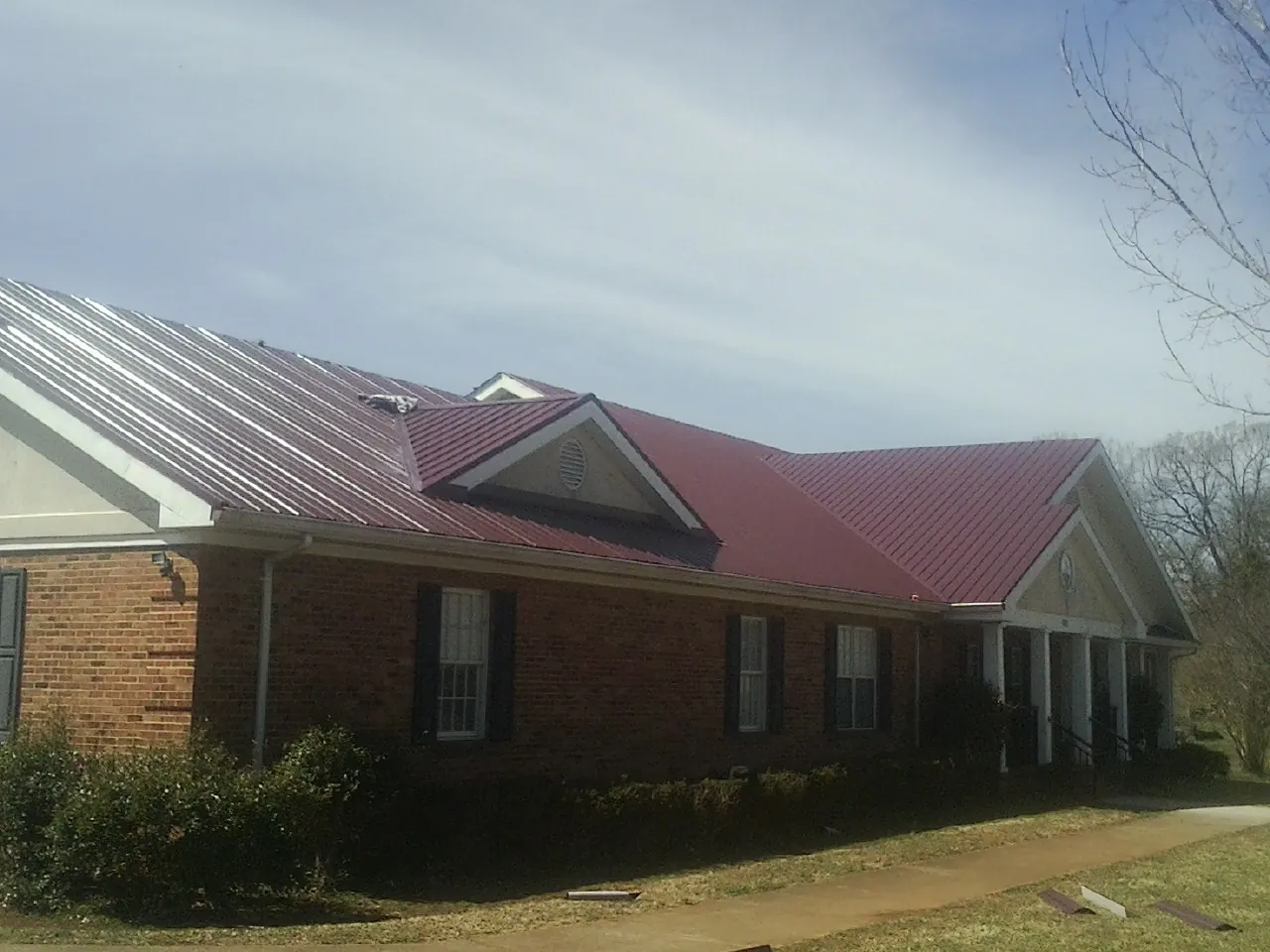 Red metal roof with gabled entries on a long brick building, from a Hail Damage Roof Repair job in Jbsa Randolph