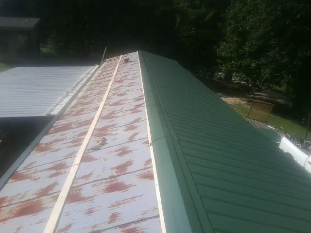 Old rusted panels beside newly installed green metal roofing — Wind Damage Roof Repair by Roofing Brothers in Jbsa Randolph