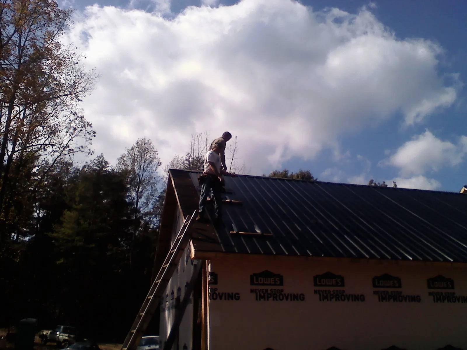 Roofer fastening dark metal panels high against a cloudy sky, from a Roof Inspection job in Jbsa Randolph