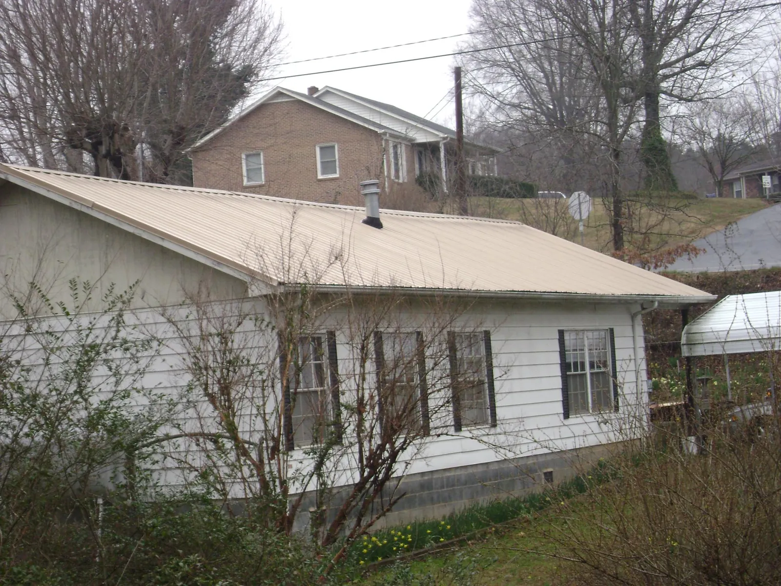 Tan metal roof on a white sided house set into a hillside — Commercial Roofing by Roofing Brothers in Jbsa Randolph